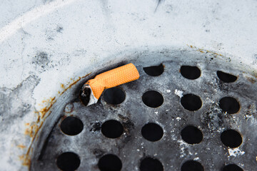 Closeup of a discarded cigarette butt stuck in a rusted metal grate of garbage bin. Nonsmoking, smoking harm, urban pollution, healthy and unhealthy lifestyle, littering, environmental concept.
