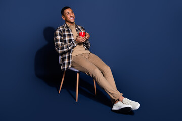 Full length photo of handsome good mood guy wear checkered shirt sitting stool drinking tea emtpy...