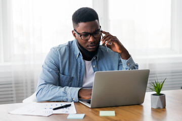 Concerned african american employee talking on mobile phone and looking at laptop screen, having issues with project, copy space