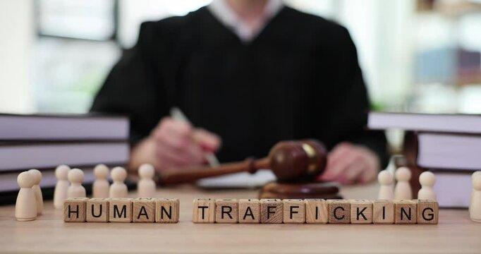 Word traffickin and figurines of little men on table of judge with gavel in courtroom. Slave trade and human trafficking and exploitation
