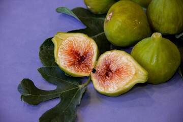 Ripe and cut green fig fruits on natural green leaves on blue background with full depth of field