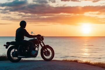 Fototapeta premium A man is riding a motorcycle on a road near the ocean. The sky is orange and the sun is setting