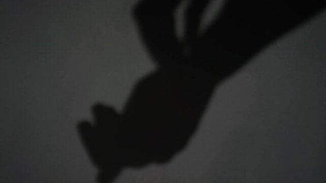 Close-up view of defocused long shadow of hands intertwining and directing downwards on grey background
