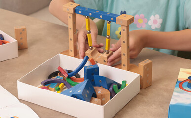 Girl assembles swing from magnetic wooden construction set. Toys and activiti children....