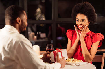 Valentine's Day. African American Man Giving A Gift To Girlfriend Having Romantic Date In Restaurant. Selective Focus