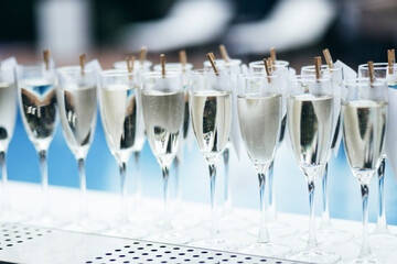 Glasses with cold sparkling wine standing on a counter in a row, swimming pool in back, party bar