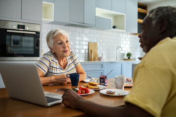 Diverse senior couple eating breakfast together on the kitchen table