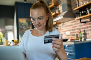 Young woman shopping online with credit card at home kitchen