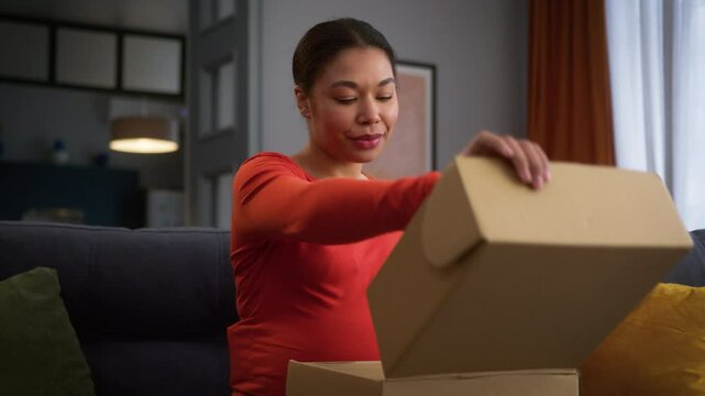 Happy mother pregnant woman African American inspired healthy ethnic girl female home couch sofa enjoy pregnancy unpacking open parcel box goods child cloth kid clothes delivery service post courier