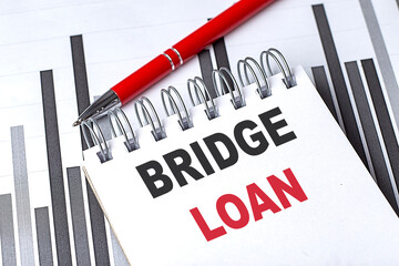 Bridge loan text on a notepad with financial charts and a red pen