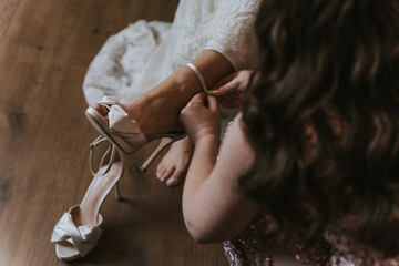 Mujer pone zapato de novia a novia antes de la boda, vemos vestido blanco nupcial