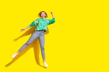 Full length photo of charming lucky woman wear green sweatshirt jumping high rising fist empty space isolated yellow color background