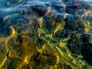 pebble bottom with large stones and seaweed through calm crystal clear transparent sea water.