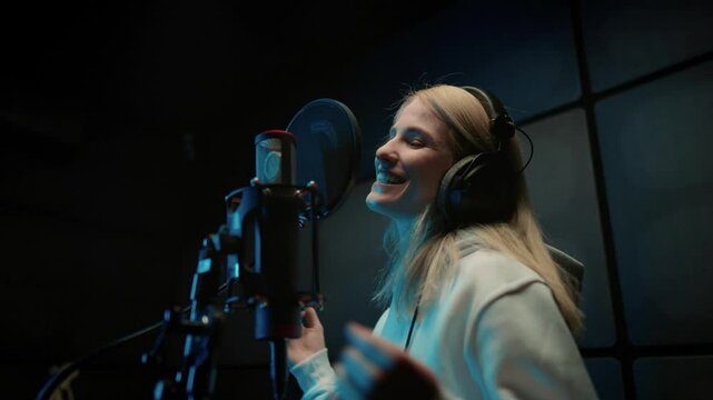 Joyful female singer performing hip-hop or rap song in modern recording studio. Portrait of beautiful Caucasian young woman singing loudly to professional microphone, record of new musical album