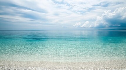 Obraz premium Serene turquoise ocean waves lapping against a white sandy beach under a partly cloudy sky.