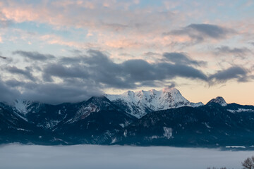 Scenic view of snow-capped mountain peak Mittagskogel (Kepa) in Karawanks at sunrise seen from Rosental, Carinthia, Austria. Cloud covered alpine landscape. Peaceful scene in Austrian Alps in winter