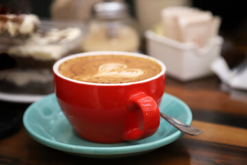 
Large cup of coffee on a bar table. Red bowl with heart-shaped latte art. Hot drink. Coffee with milk. Cappuccino.