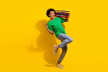 Full length photo of handsome good mood guy wear green t-shirt show v-sign enjoy boom box songs emtpy space isolated yellow color background