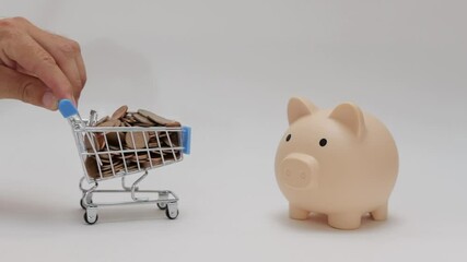 Close-up view of  hand placing coins from shopping cart into piggy bank against clean white background, symbolizing saving and financial management
