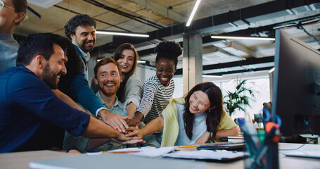 Multi-ethnic team placing their hands on top of each other and raising them together afterwards. Man in middle clapping with joy. Positive ending after team building process. People going back to work