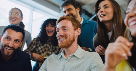 Obraz premium Multi-ethnic group of people at work. Looking patiently at screen. Waiting for important moment. After seeing positive result everyone exclaiming. Clapping their hands while smiling with joy.