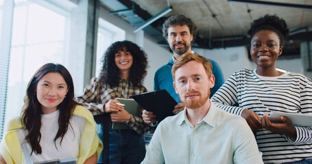 Positive multi-ethnic team working together at one desk. Portrait of diverse group looking at camera and smiling.