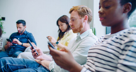 Side view of people sitting on couches while waiting for their turn. Spending time in smartphones....