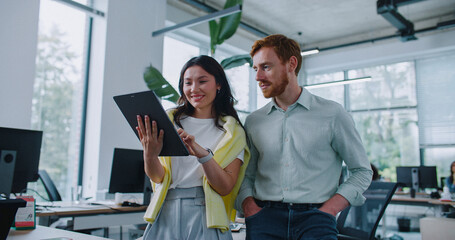 Happy young woman spending coffee break with her colleague in office. Female holding tablet device...