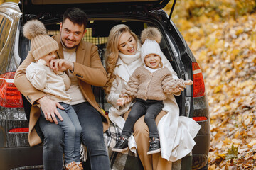 Young family sitting at open trunk of hatchback car in autumn forest