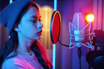 Woman singing into a microphone in a brightly lit recording studio environment with professional...