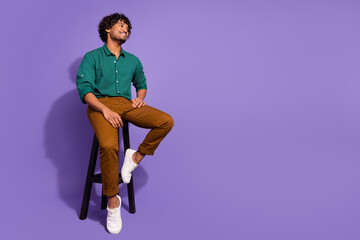 Full body length photo of handsome hispanic guy in bar chilling out sitting stool looking novelty isolated on violet color background