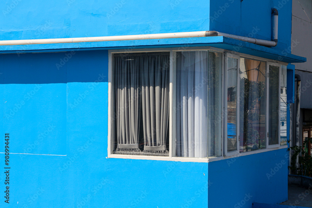 Aufkleber a blue building with a window on the side and a large bay window and white curtains on the corner of