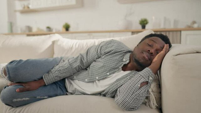 Daytime sleep, young adult African man relaxing on sofa in apartment, take a nap . Relaxation in afternoon, lazy weekend, black male person lying on couch and dreaming, recovery energy and vitality