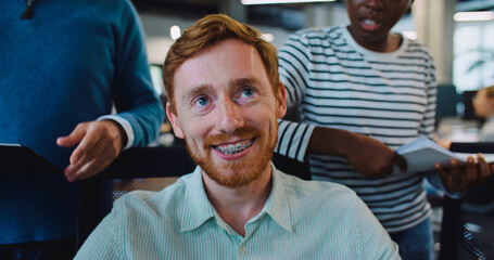 Camera focus on handsome Caucasian man with red hair and moustache. Male trying to explain something to work colleagues and smiling.