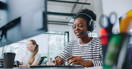 Camera view of diverse women sitting in front of computer displays. Worker on right side and wearing headset for remote consultation with clients. Working in call center. Customer support.