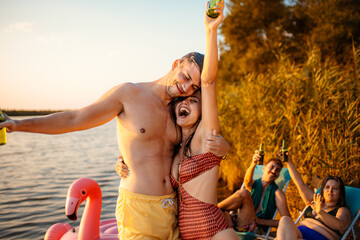 Portrait of a couple in swimsuit having fun standing on a pier drinking beer with they friends on...
