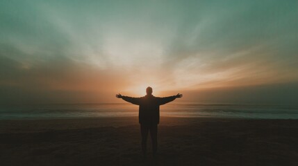 Fototapeta premium Man with arms outstretched standing on the beach and looking at the sunset.