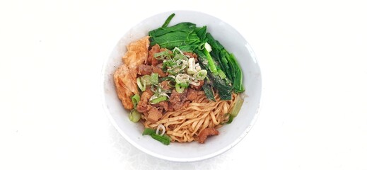 Chicken noodle or mie ayam with fukien, fried dumplings and vegetables served on bowl isolated on white background. Popular street food in Indonesia