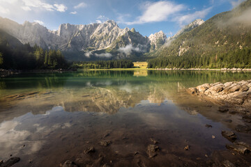 Scenic morning view on Lago di Fusine near border between Italy and Slovenia. Charming lake with amazing deep colorful water and foggy forest around it.