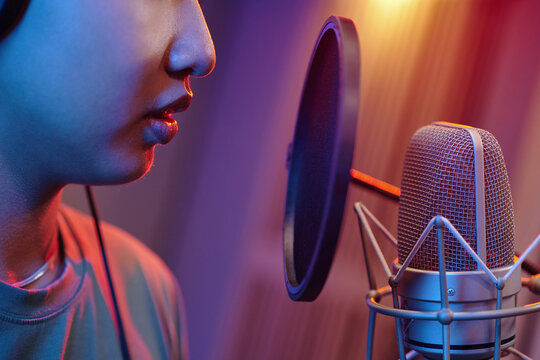 Close-up of person recording audio in professional studio setting with high-quality microphone. Focus on mouth and microphone, highlighting details of equipment used