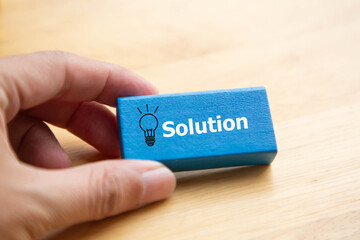 Concept of Business solution and idea; Hand holding solution word and light bulb symbol on wooden block