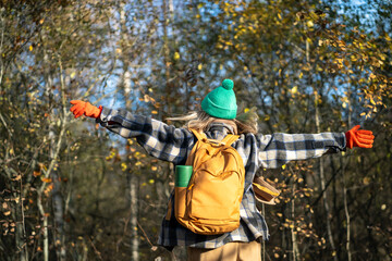 Naklejka premium Contented woman traveler having good time outside, enjoying wandering in autumn forest. Female tourist backpacker scrolling in sunny fall weather outside. Nature therapy, stress free, break from city