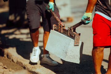Workers with a Block Clamp Holding Heavy Concrete Curb Blocks. Constriction manual laborers working...