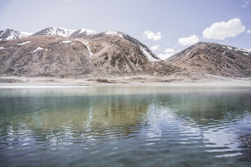 High-mountain lake Khargush with snow and ice on the surface of the water against the backdrop of mountain rocky peaks with snow in the Tien Shan mountains in Pamir in Tajikistan, landscape