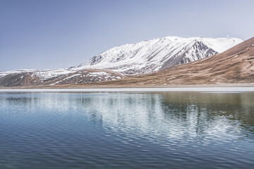 High-mountain lake Khargush with snow and ice on the surface of the water against the backdrop of mountain rocky peaks with snow in the Tien Shan mountains in Pamir in Tajikistan, landscape