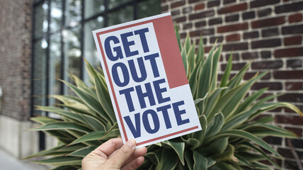 Get out vote flyer held in hand near green plant, promoting civic engagement and participation in elections. This image captures essence of encouraging voter turnout