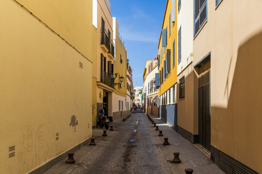 Fototapeta Narrow, picturesque streets of Seville, Spain, featuring colorful buildings, traditional architecture, wrought-iron balconies, and a peaceful urban atmosphere.