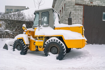 A bulldozer for clearing roads of snow during a snowfall. A bulldozer with large wheels for road construction works stands in a snowdrift in winter. Road equipment.
