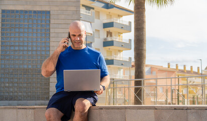 A man working with a laptop and talking on phone,  sitting in an urban setting, freelancer digital...