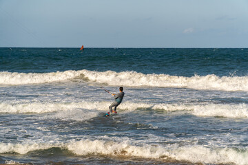 A young man kitesurfing at sunset in the sea.